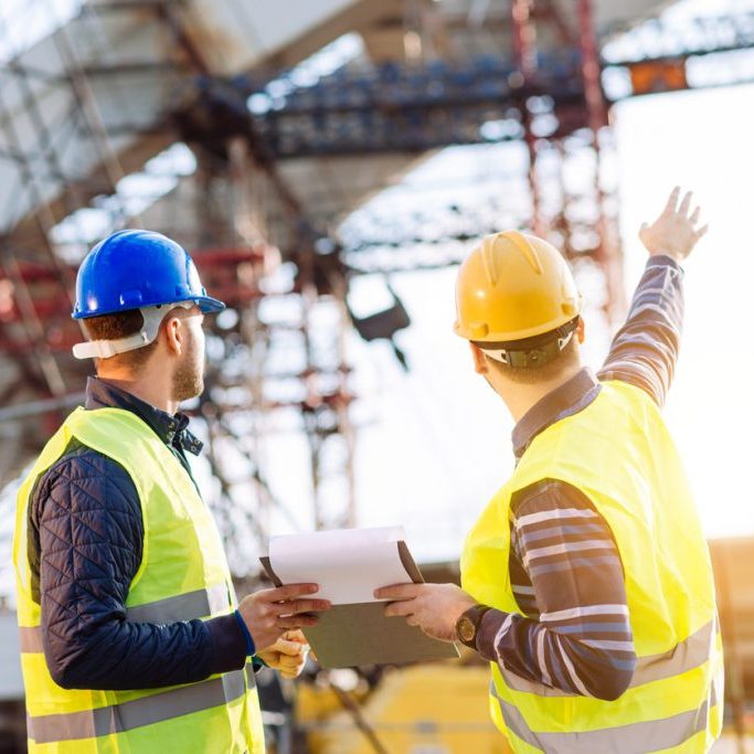 Reporting to contractor at construction site Two experts engineers in protective helmets and fluorescent vests showing the construction site and building activities after the successful project phase. Image taken with Nikon D800 and 85mm developed from RAW in XXXL size, in Novi Sad, Serbia, Central Europe, Europe