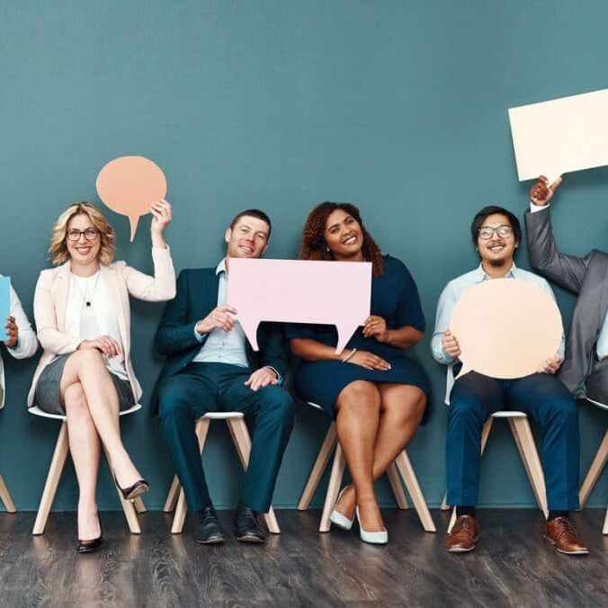 Shot portrait of a diverse group of businesspeople holding up speech bubbles while they wait in line